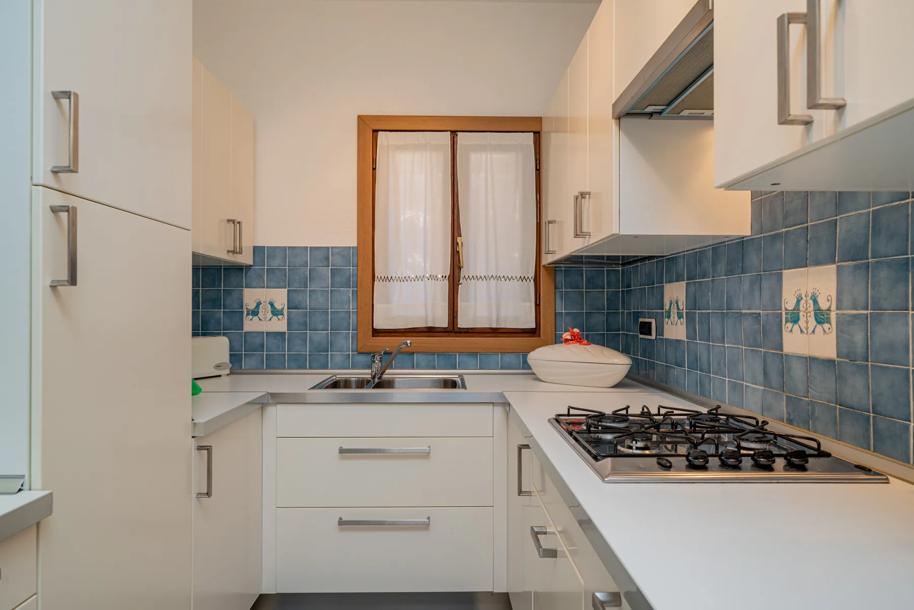Una cocina con armarios blancos, paredes de azulejos azules y una placa de gas.