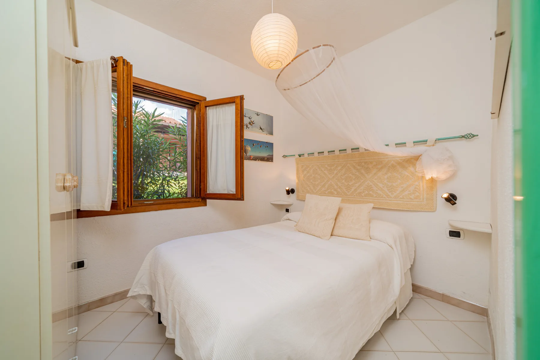 A bedroom with a white bed beneath a hanging mosquito net.