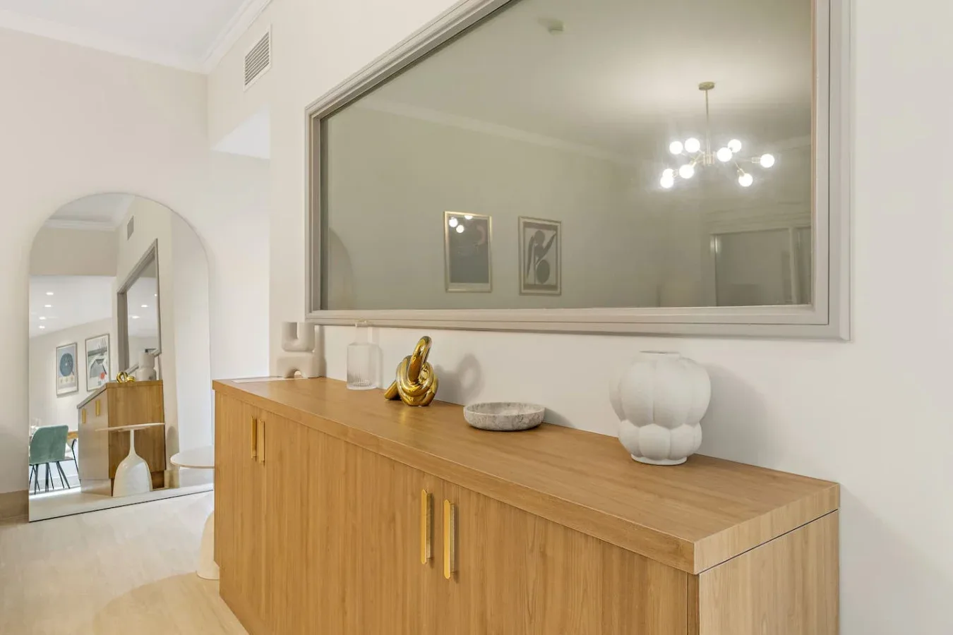 Un mueble de madera bajo un espejo grande en un interior luminoso.