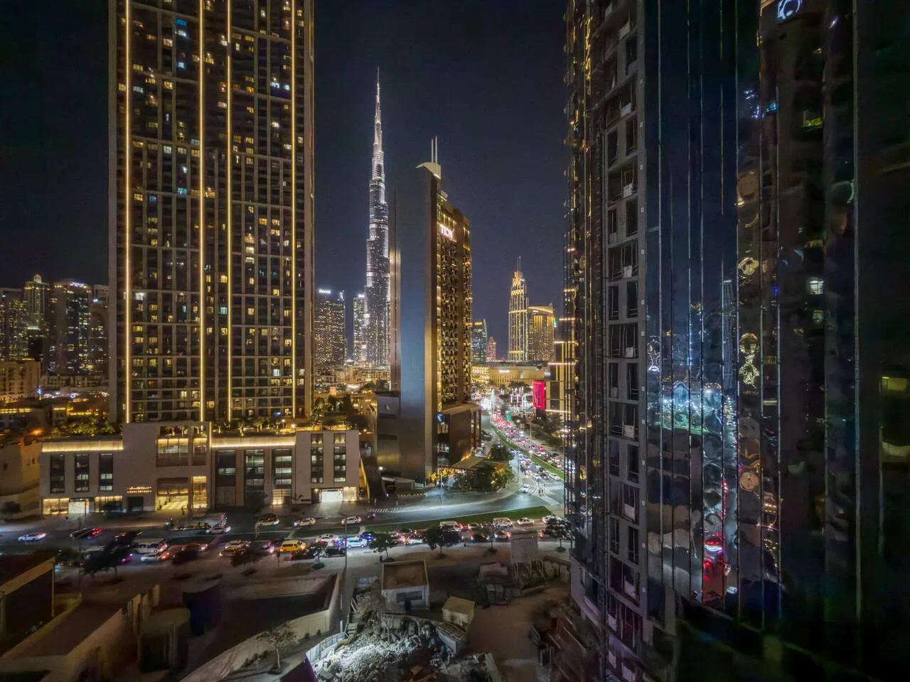 Un horizonte urbano nocturno entre edificios altos, con vías iluminadas abajo.