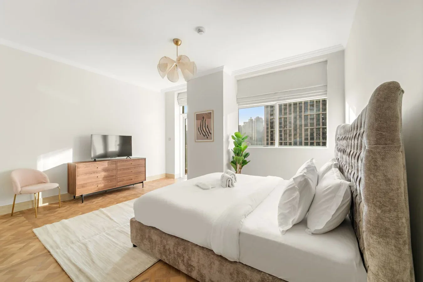 Un dormitorio luminoso con una cama tendida, un televisor y una planta en maceta.