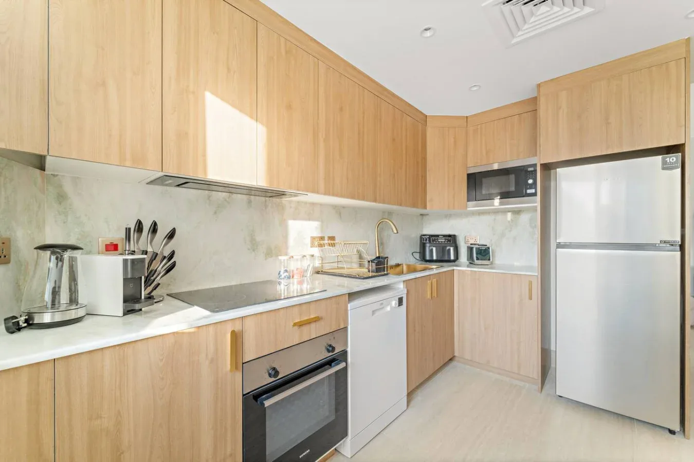 Una cocina luminosa con gabinetes de madera clara, una encimera y electrodomésticos de acero inoxidable.