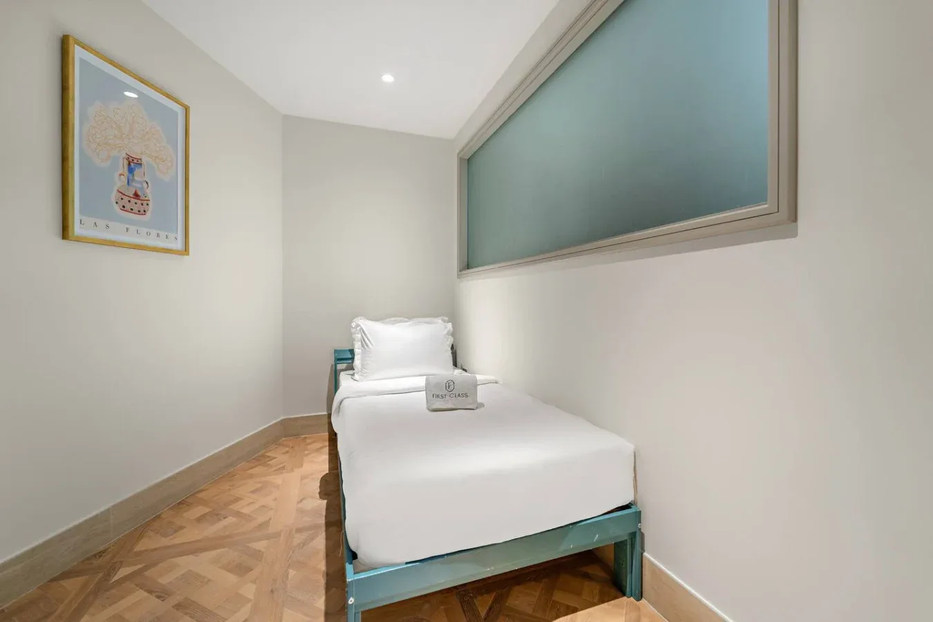 Una cama individual está bajo una ventana alta de vidrio esmerilado en un dormitorio compacto.