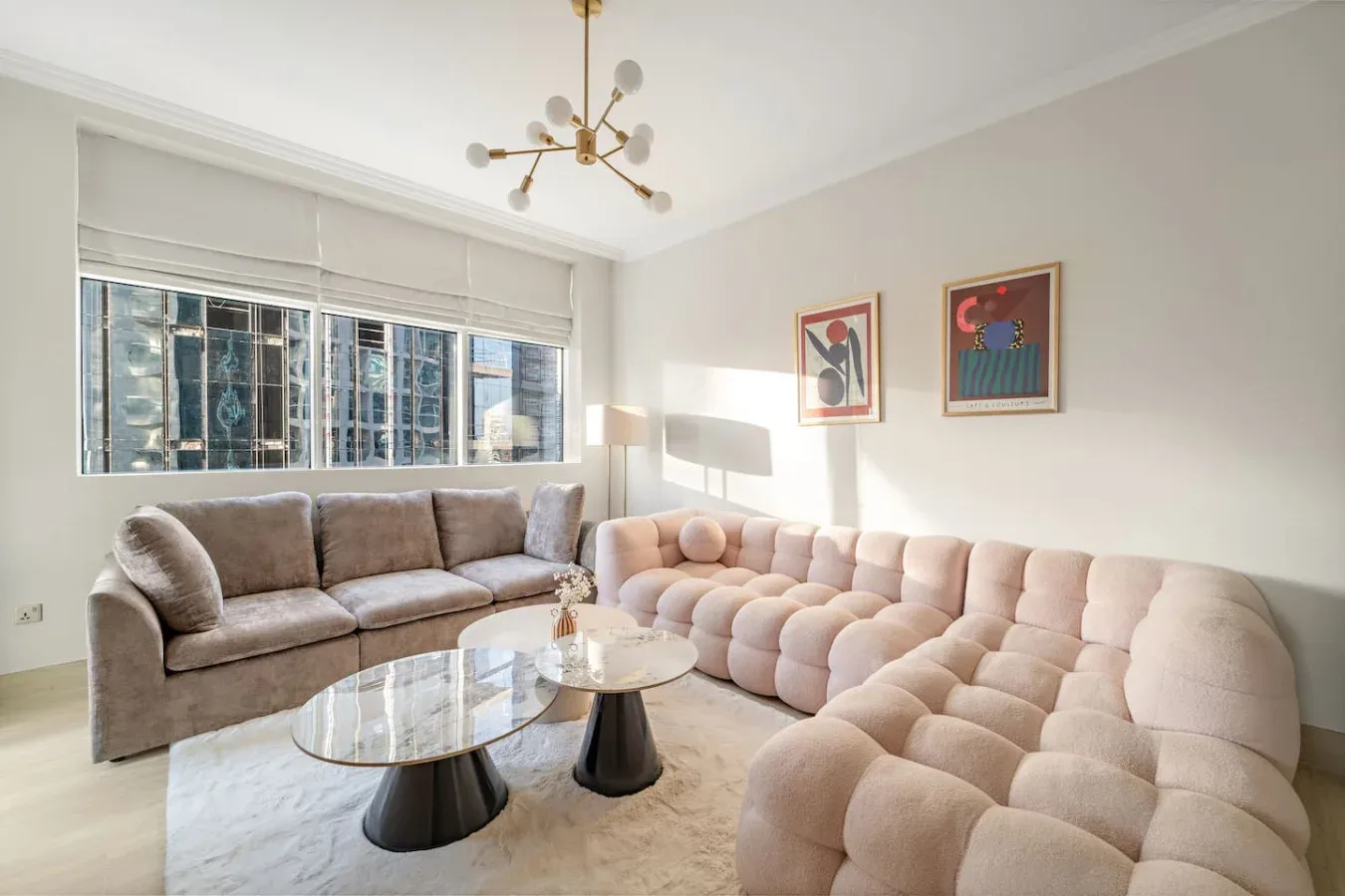 Una sala luminosa con un sofá gris, asientos modulares claros y una mesa de centro de vidrio.