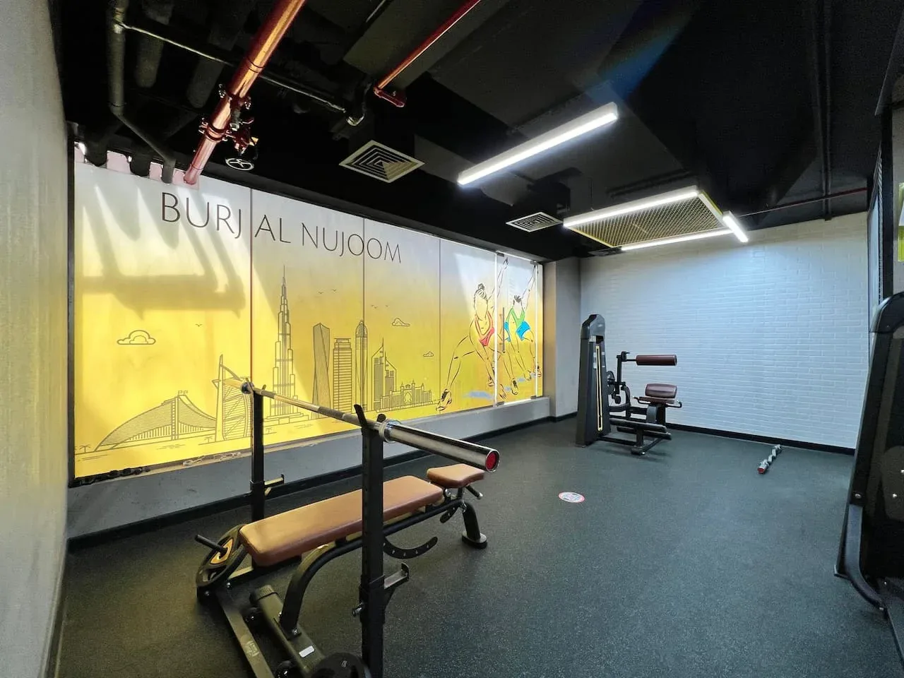 Un gimnasio con bancos de pesas y equipo de ejercicio junto a un mural.