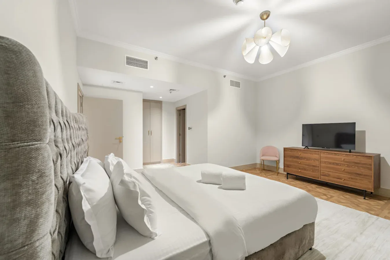 Un dormitorio luminoso con una cama grande y un televisor sobre una cómoda de madera.