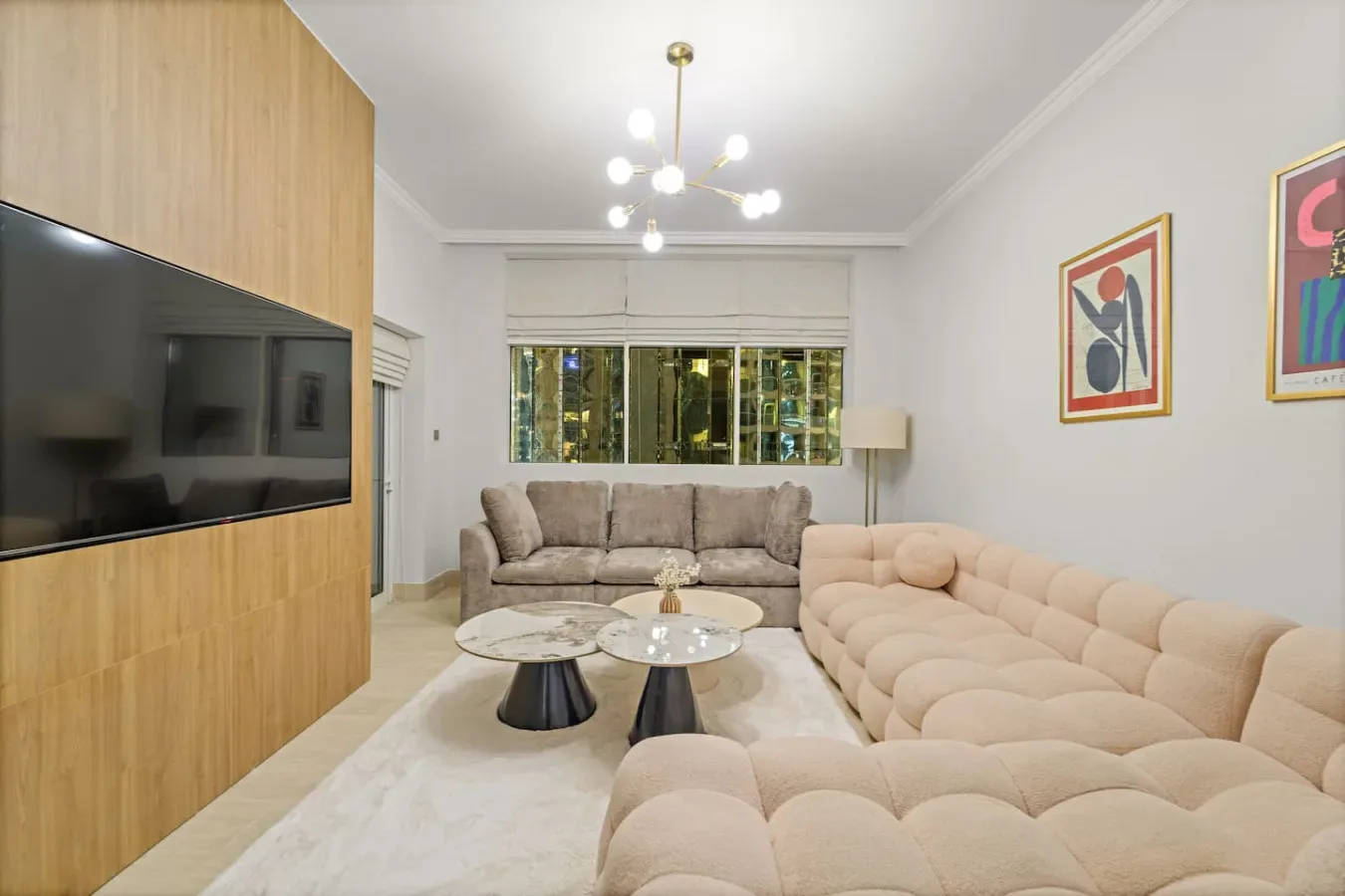 Una sala de estar con asientos acolchados, un televisor en la pared y obras de arte.