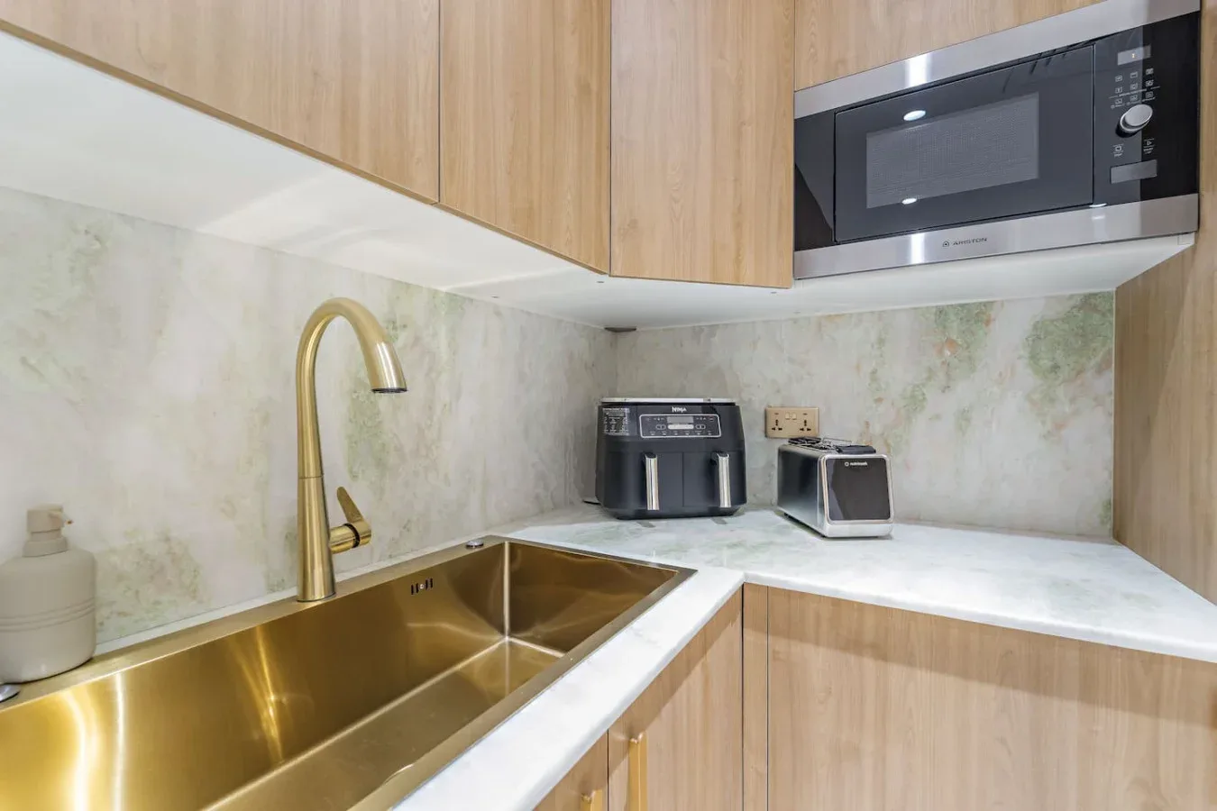 Una cocina compacta con fregadero de latón, pequeños electrodomésticos y armarios de madera clara.