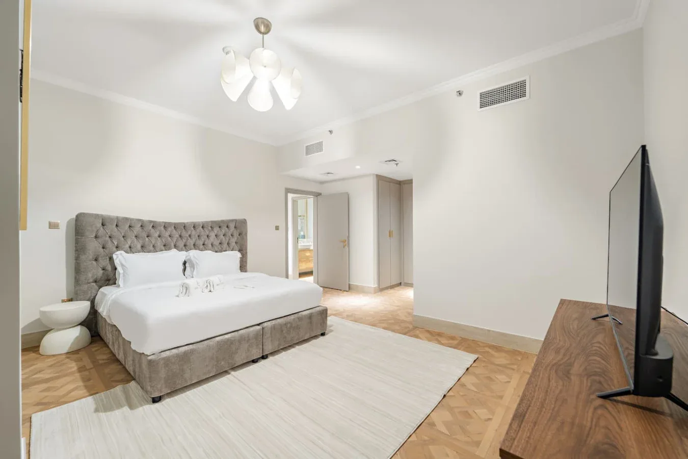Un dormitorio con una cama, una alfombra clara y un televisor.