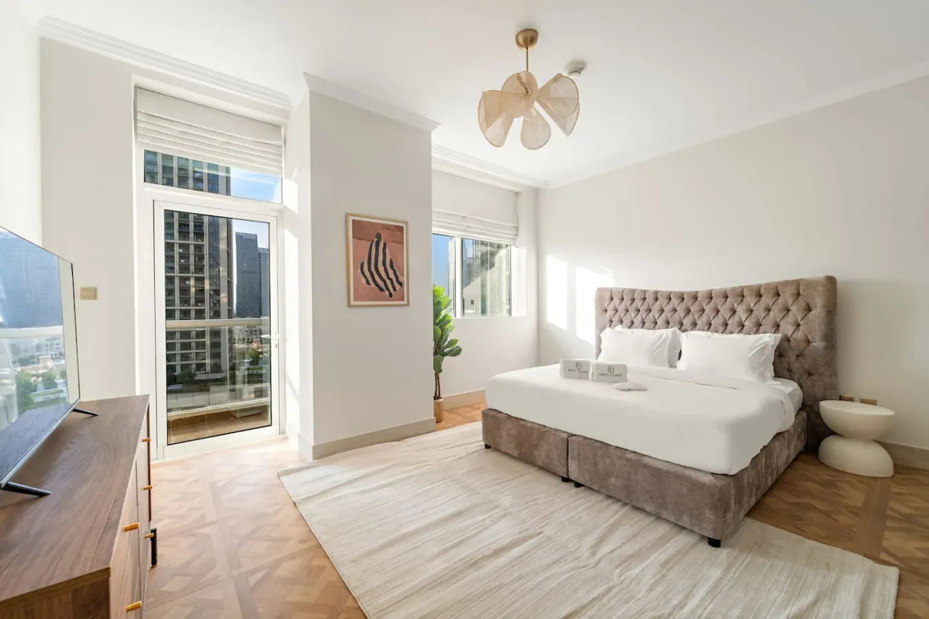 Un dormitorio luminoso con una cama, ventanas altas y una alfombra clara.