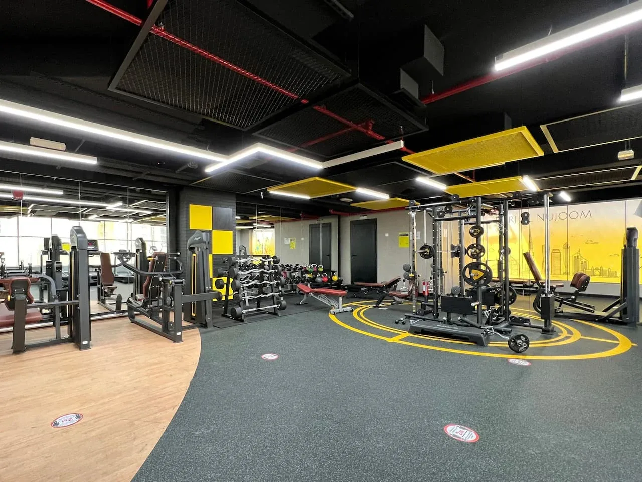 Un gimnasio con equipos de pesas, máquinas de ejercicio y marcas amarillas en el suelo.