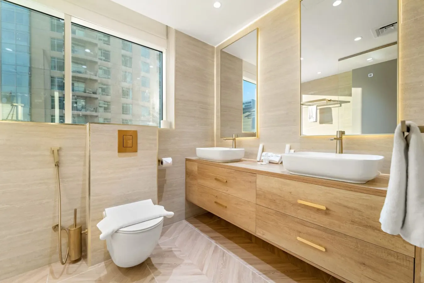 Un baño luminoso con un largo mueble de madera, lavabos e inodoro.