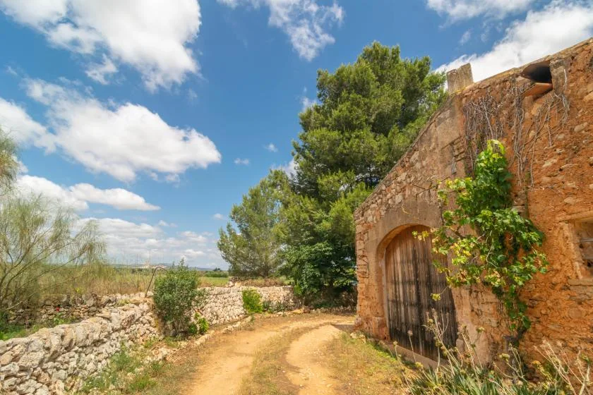 A rustic stone entrance opens beside a winding dirt path and trees.