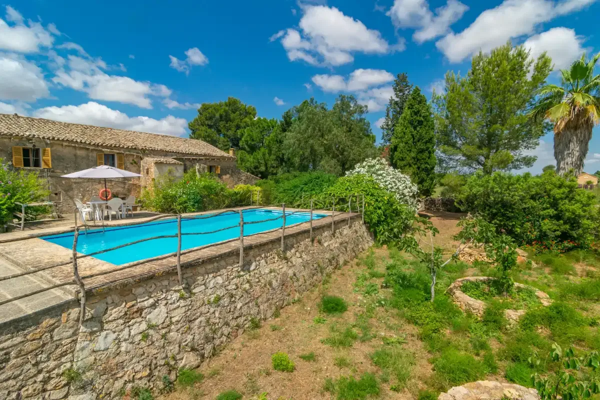 An outdoor swimming pool sits beside a stone building and landscaped greenery.