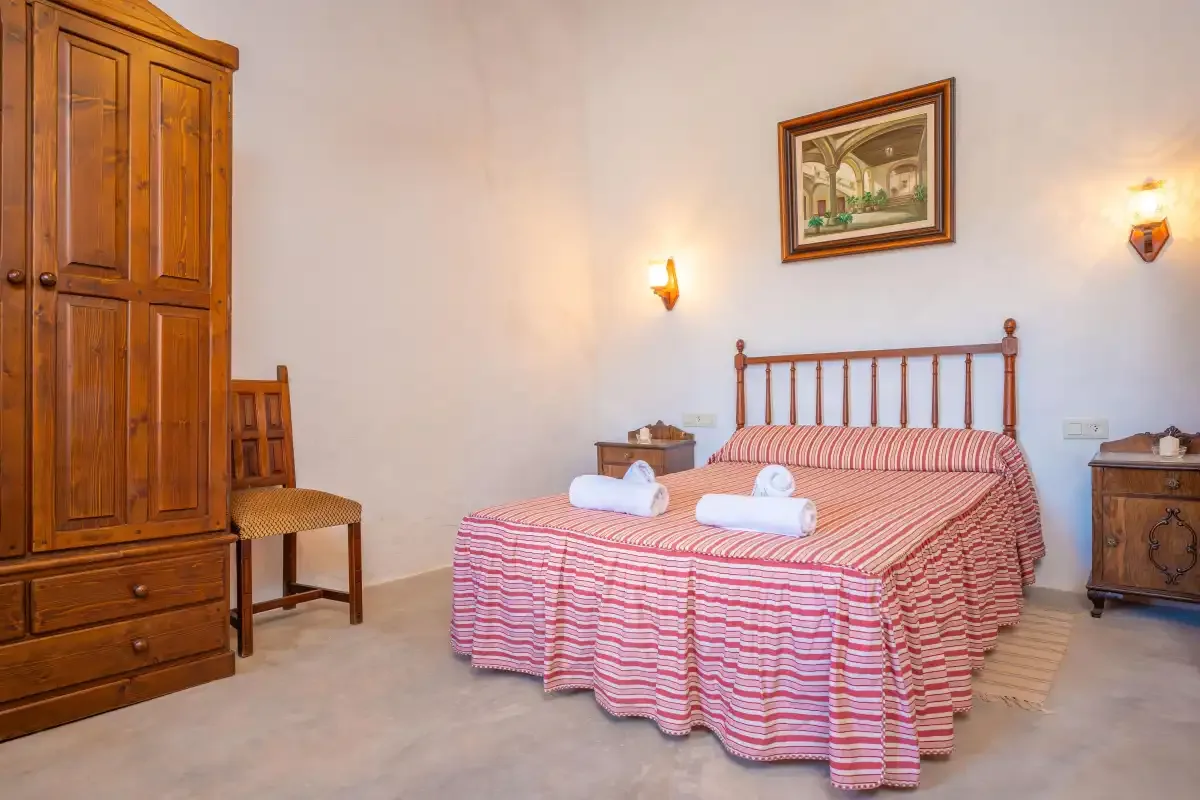 A bedroom with a striped bedspread, wooden wardrobe, and bedside lighting.