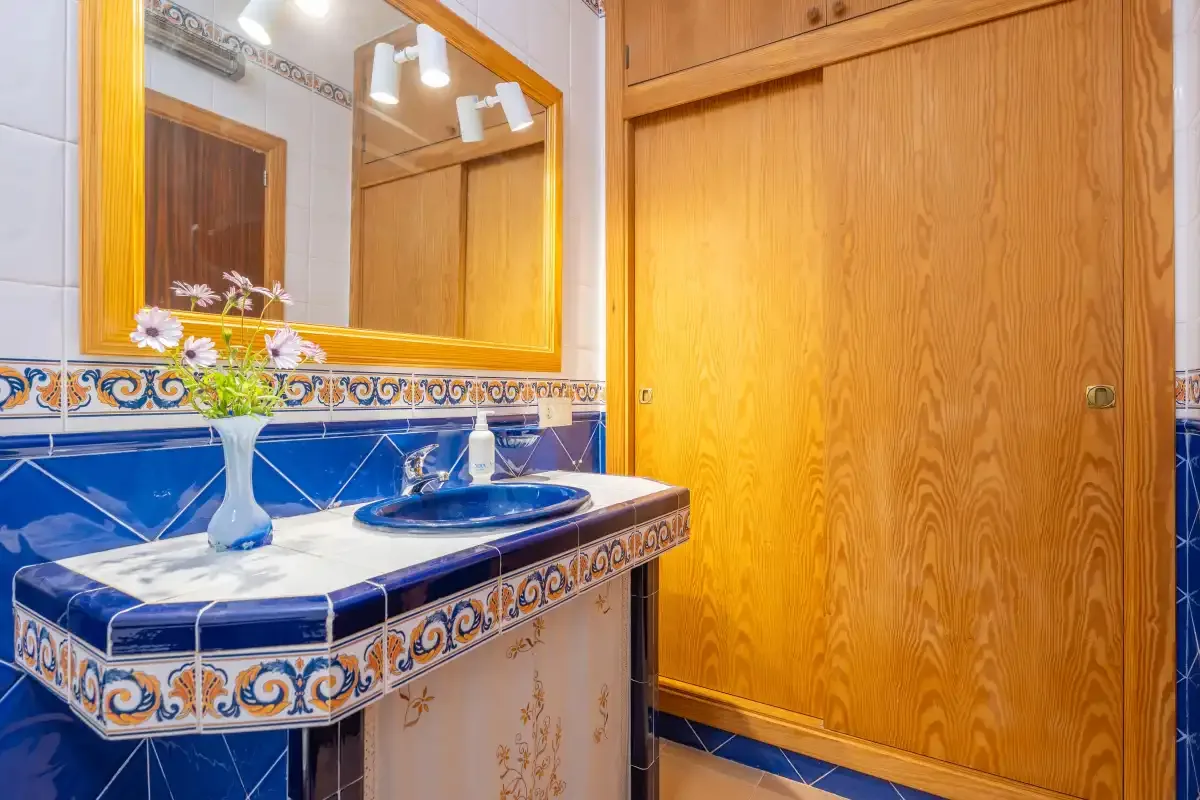 A tiled bathroom vanity with a sink, mirror, and wooden door.