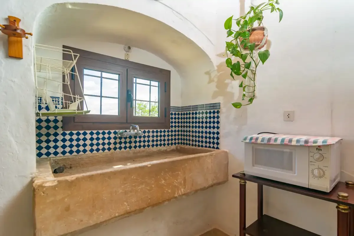 A rustic kitchen sink sits beneath a window beside a small countertop appliance.