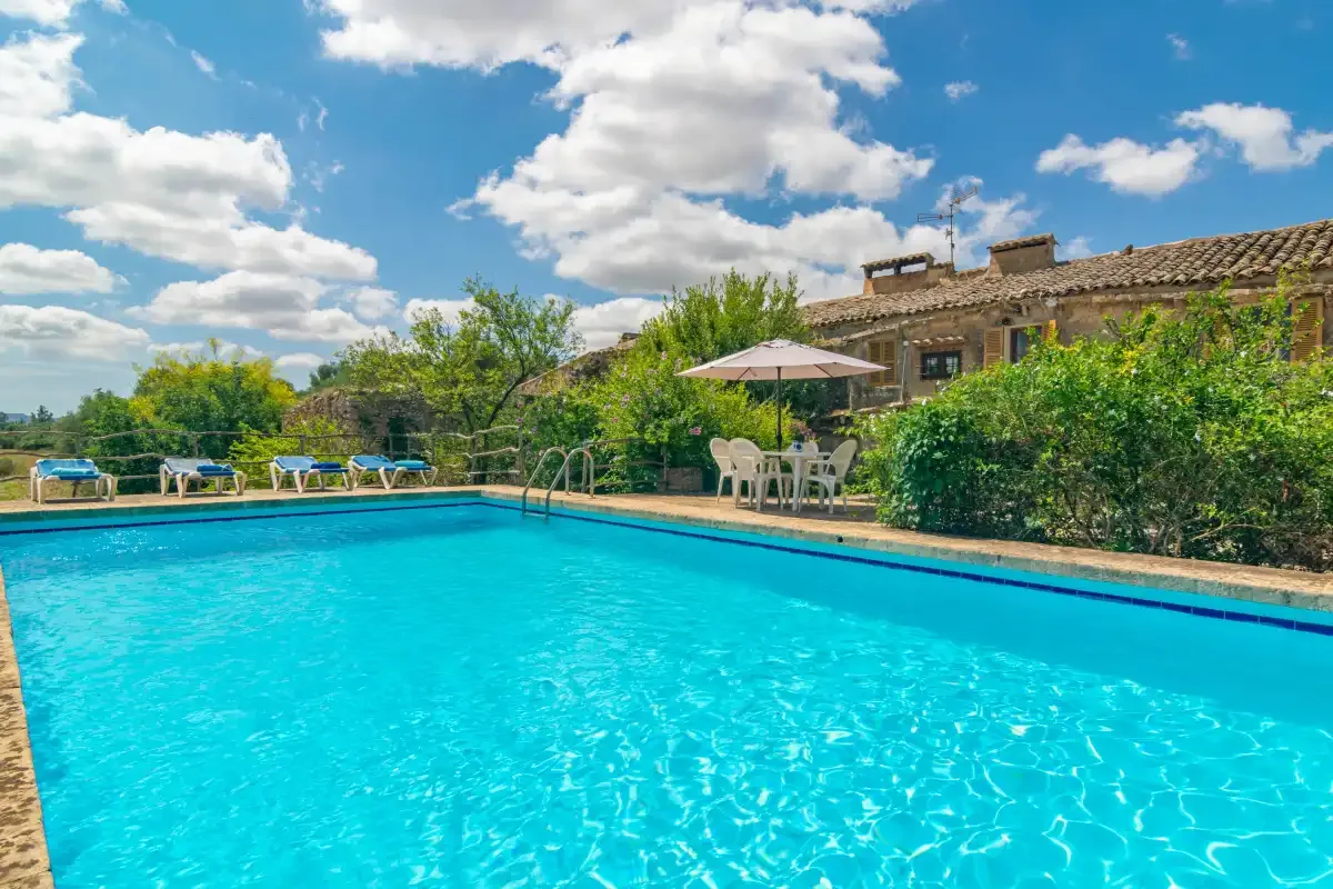 An outdoor swimming pool beside a house, with patio seating under an umbrella.