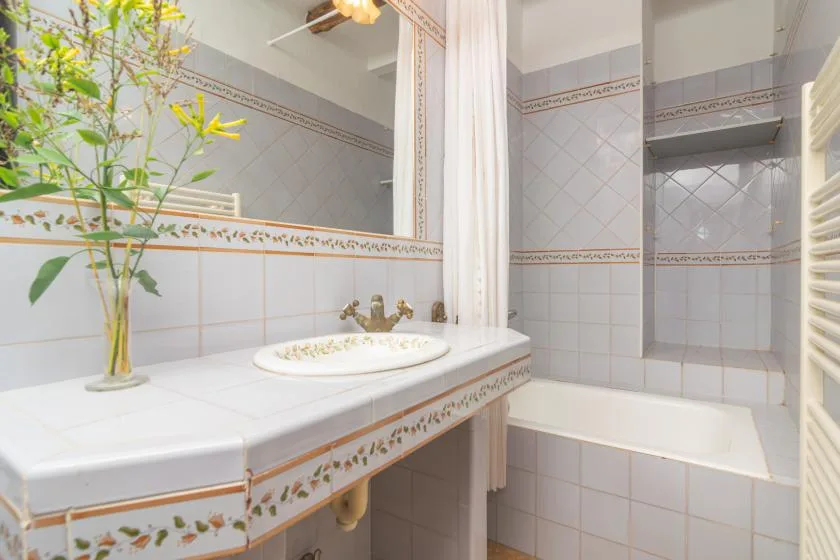A tiled bathroom with a sink, bathtub, and white shower curtain.