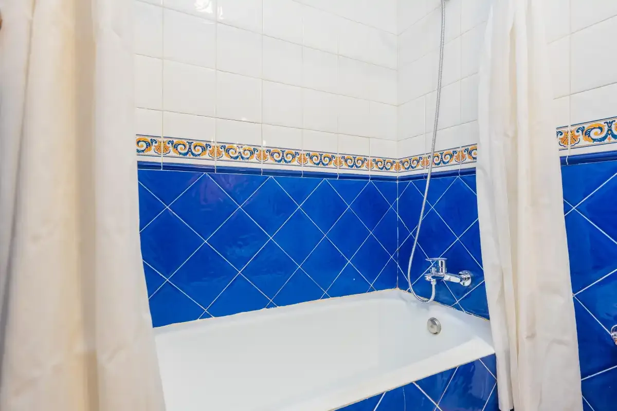 A bathtub with a shower fixture is set against blue and white tiled walls.