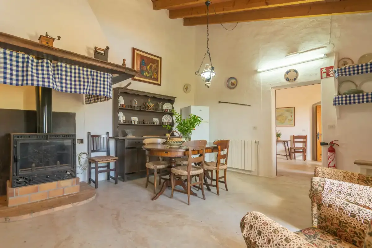 A rustic dining and living area with a wooden table and chairs beside a fireplace.