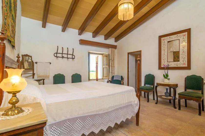 A bedroom with a large bed, chairs, and exposed wooden ceiling beams.