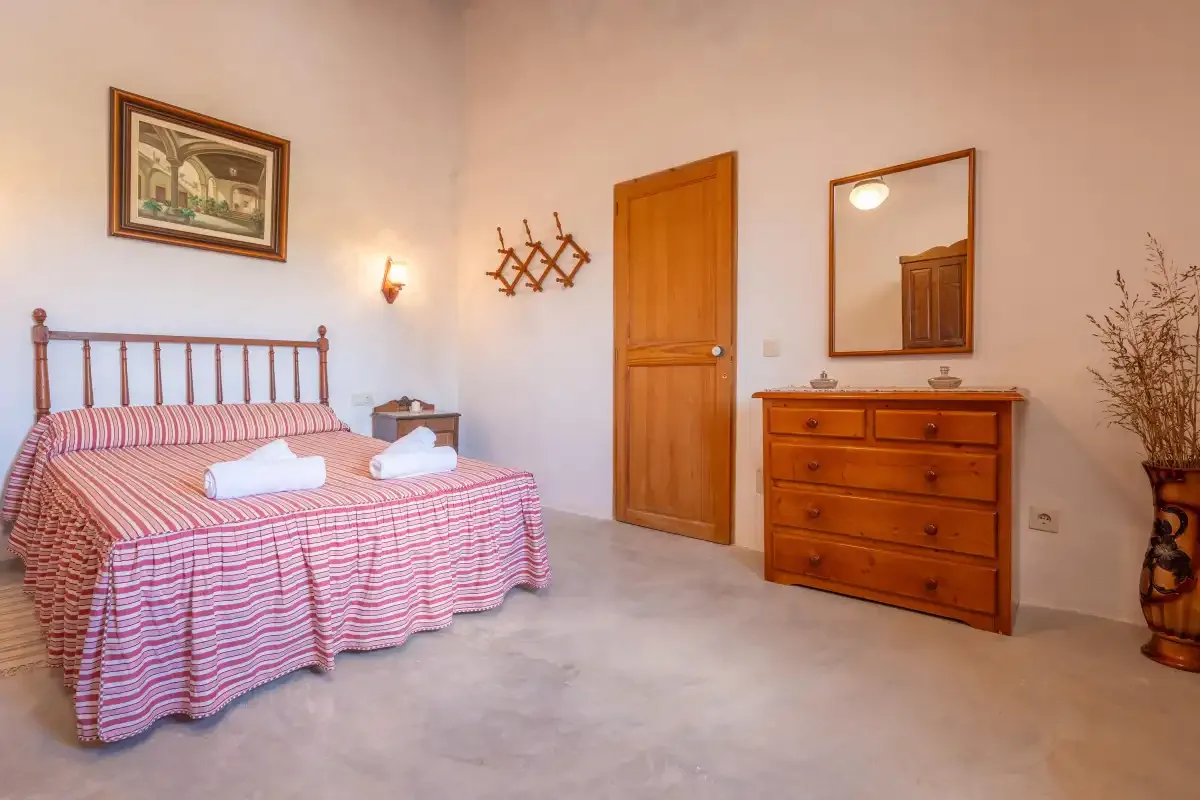 A bedroom with a double bed, wooden dresser, and mirror.