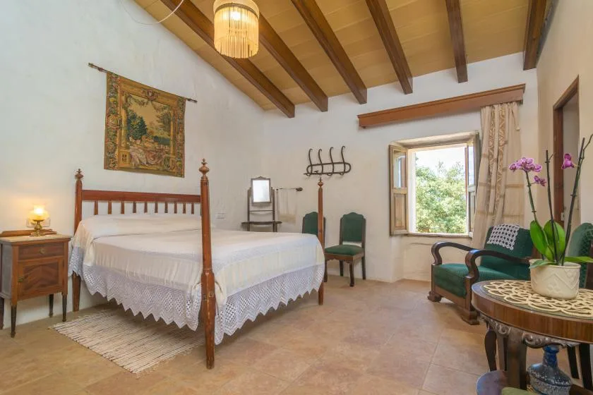 A bedroom with a wooden bed, green seating, and a window overlooking greenery.