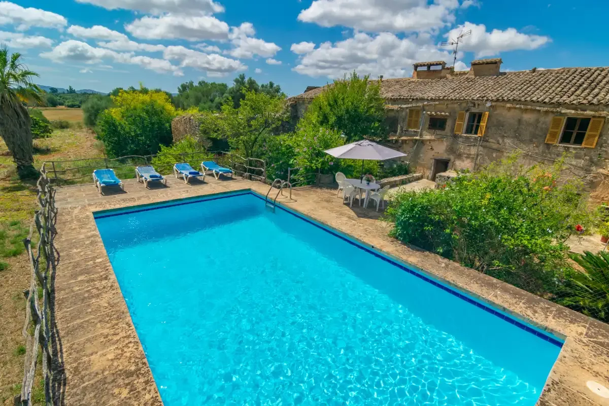 An outdoor swimming pool beside a stone building and surrounding greenery.