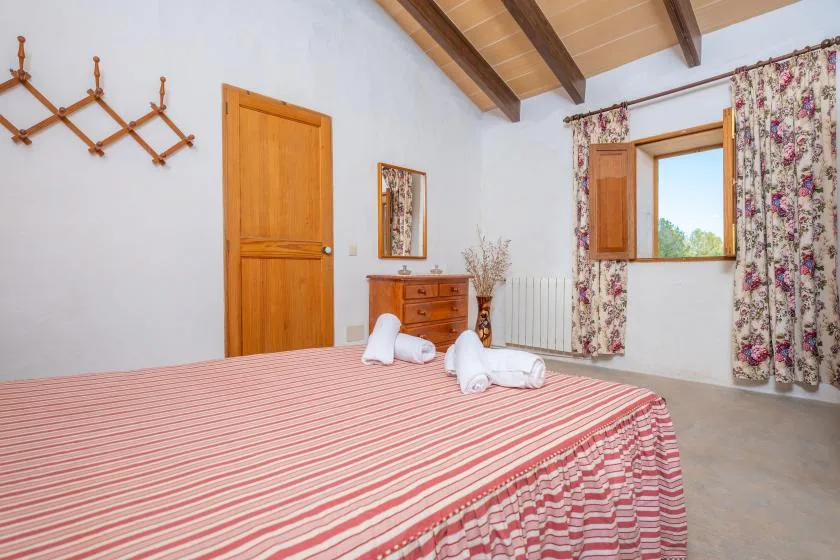 A bedroom with a striped bedspread, wooden furniture, and an open window.