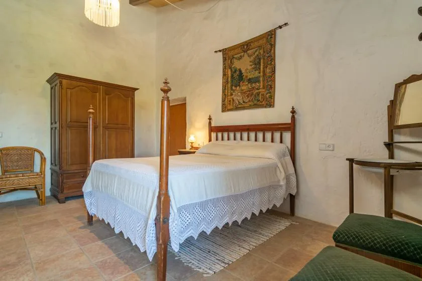 A bedroom with a wooden four-poster bed and a tapestry on the wall.