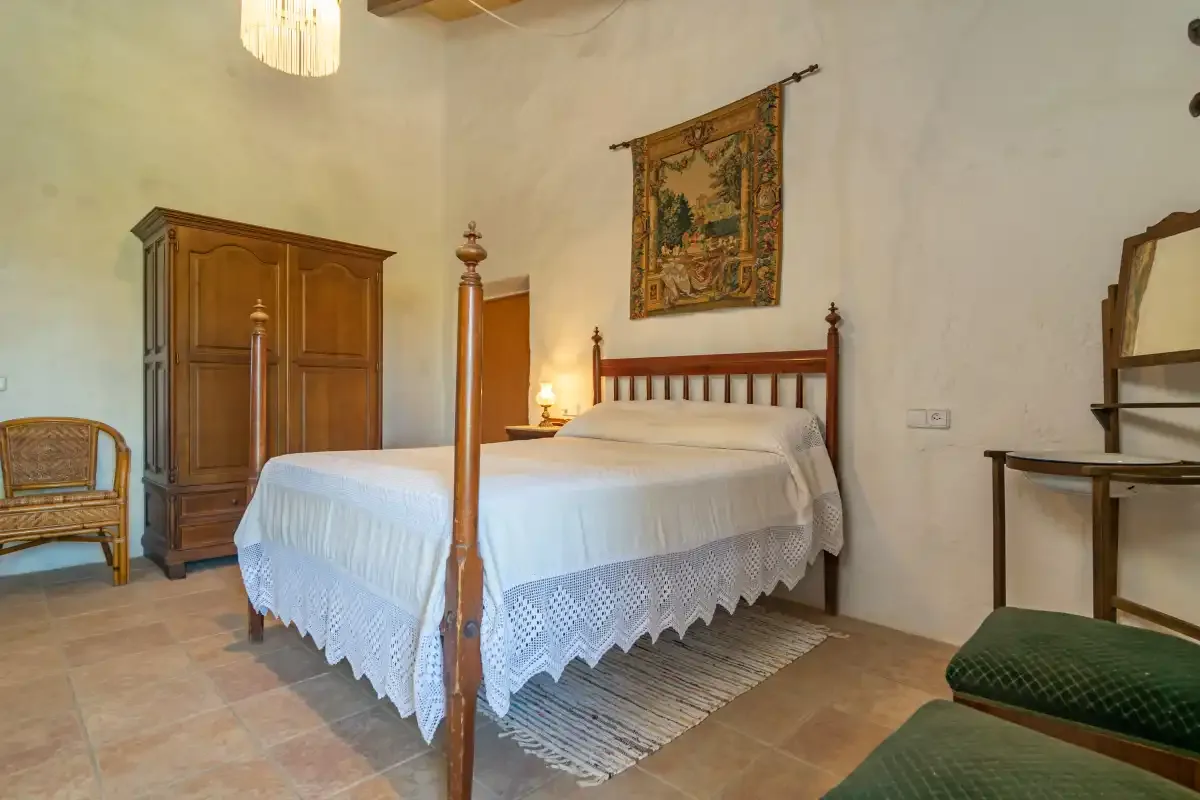 A bedroom with a wooden four-poster bed, a wardrobe, and a chair.
