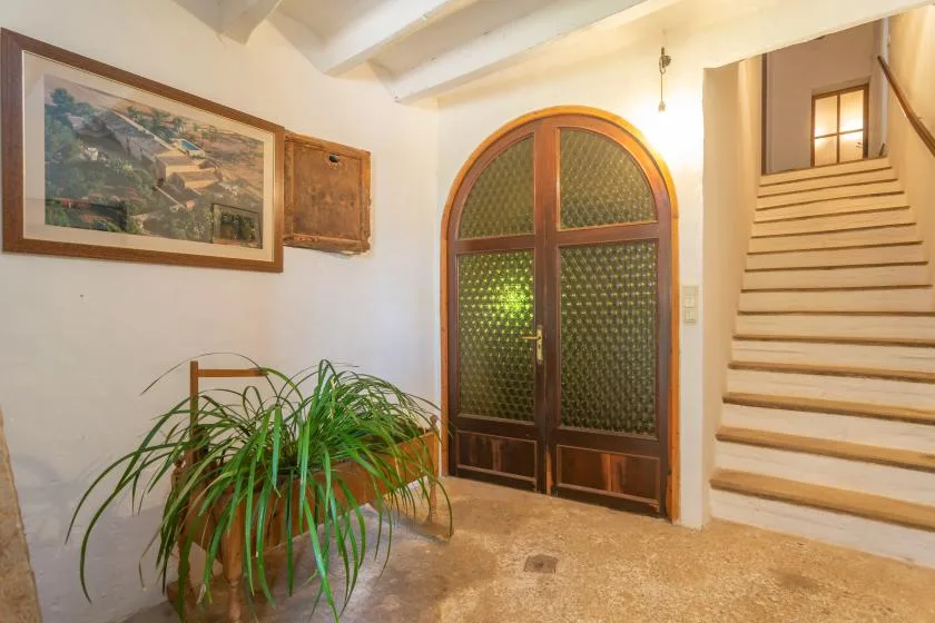 A bright interior hallway with an arched wooden door and staircase.