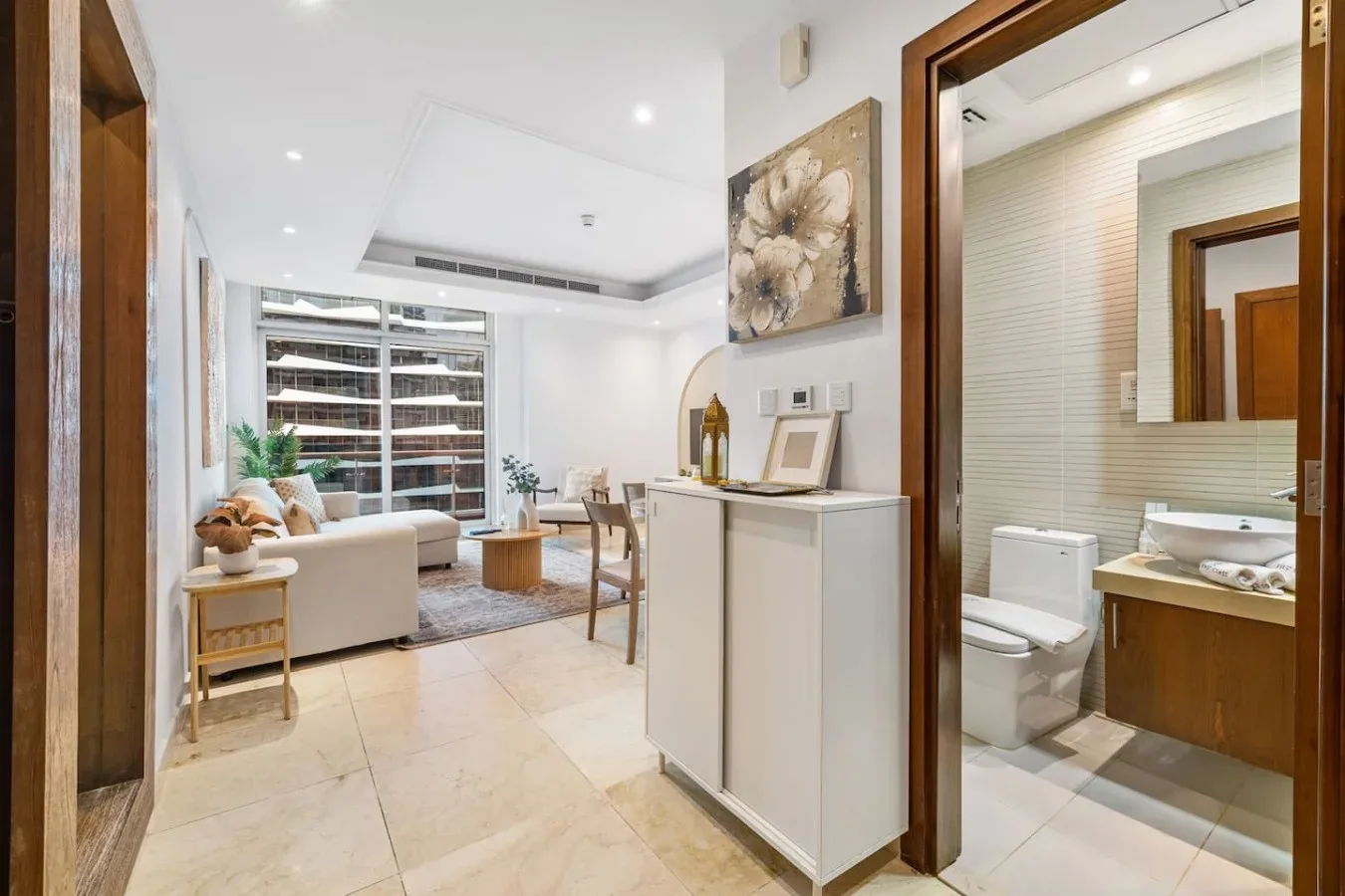 Una luminosa sala de estar junto a un baño, con asientos y una consola.