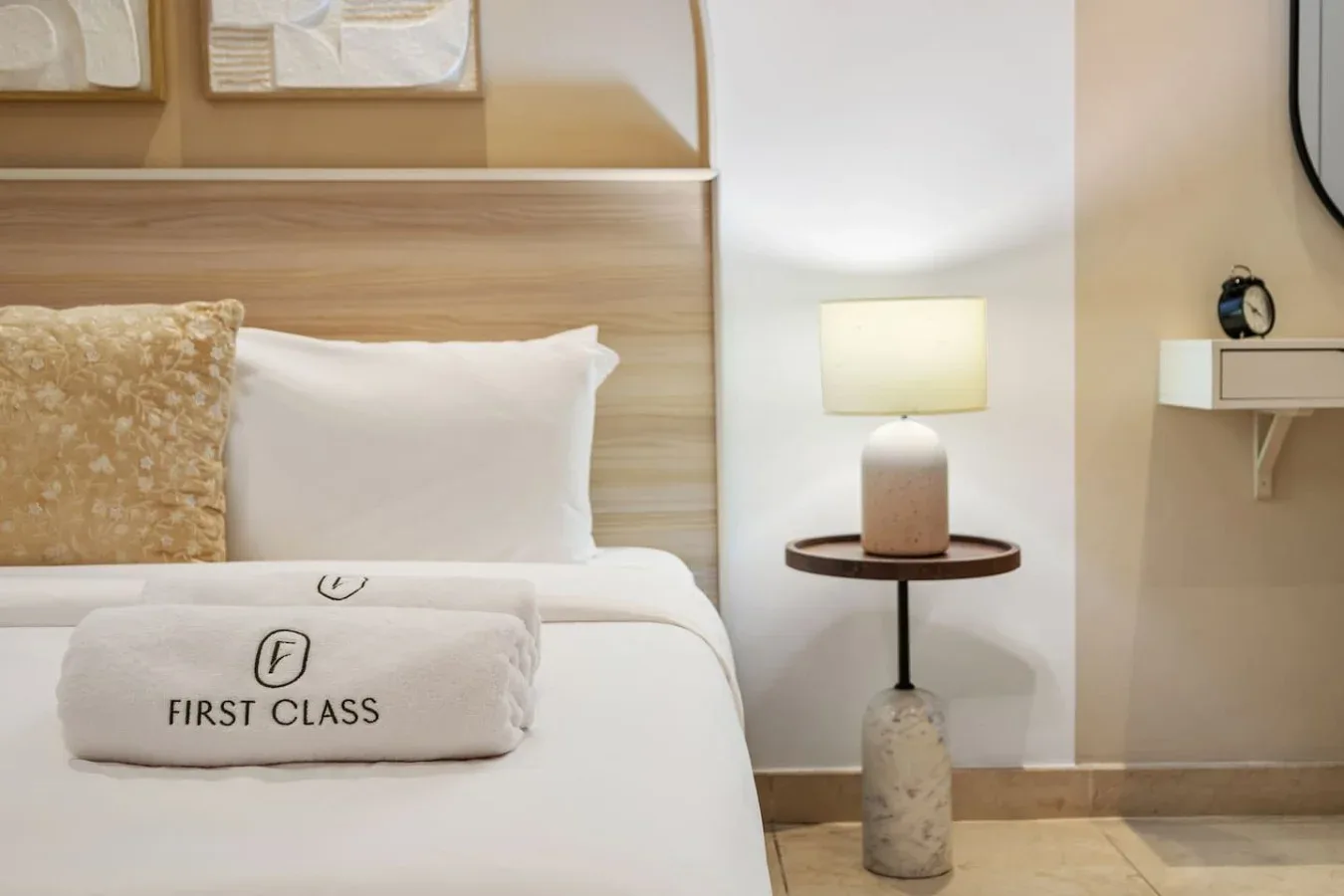 Una cama bien arreglada con almohadas y una toalla doblada junto a una lámpara.