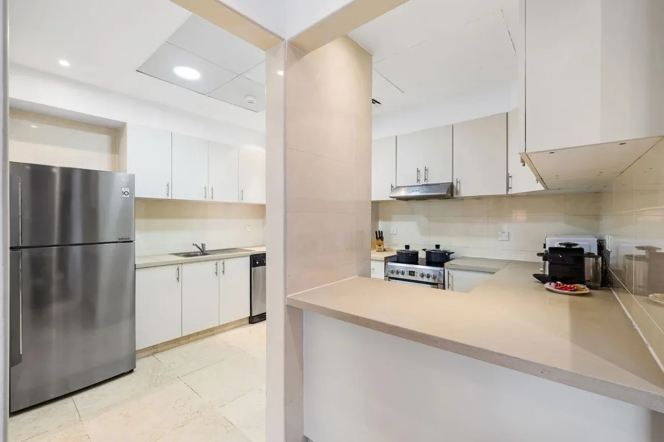 Una cocina luminosa con gabinetes blancos, un refrigerador y una amplia encimera.