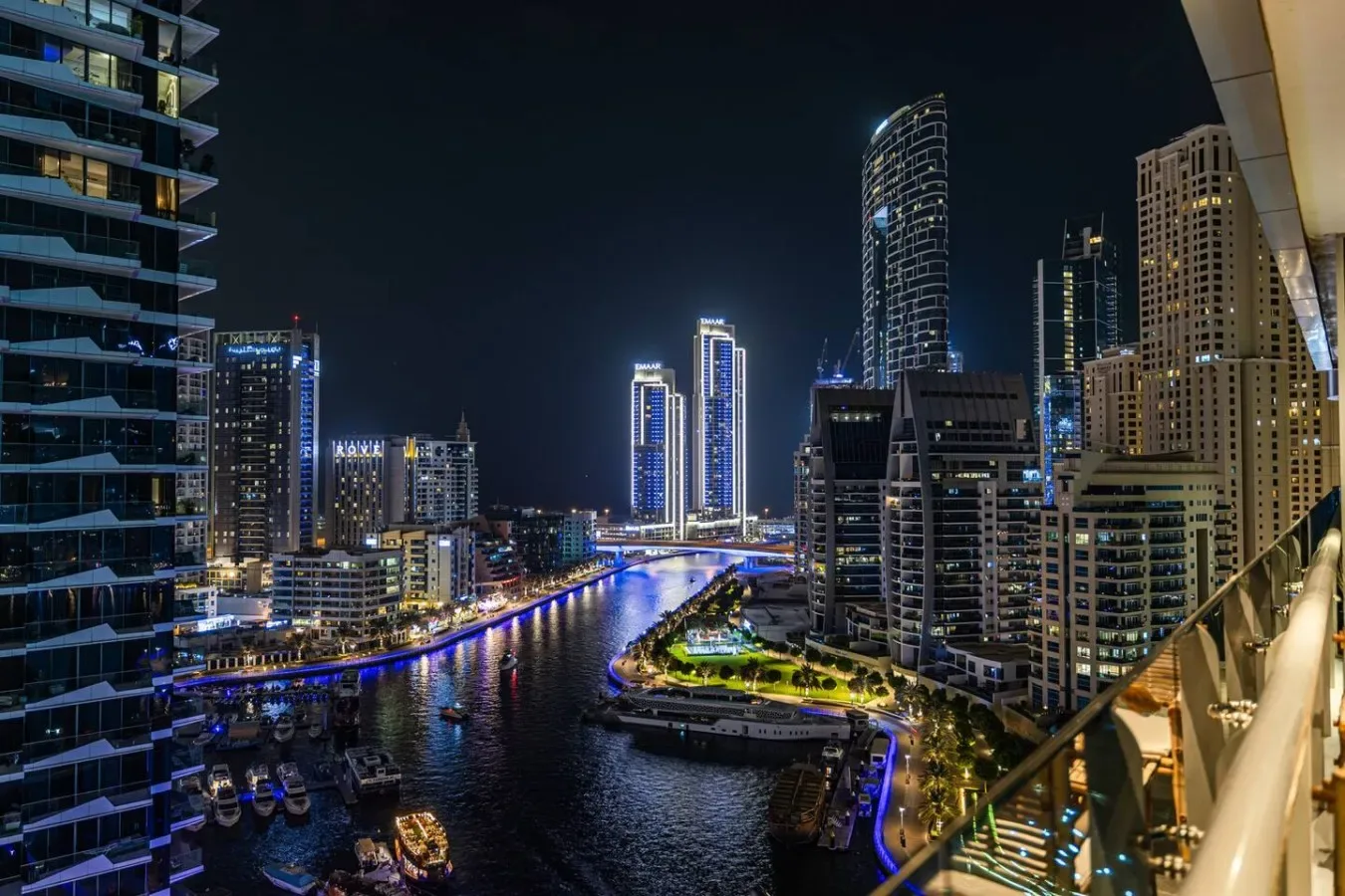 A nighttime city skyline rises above a canal lined with illuminated buildings.