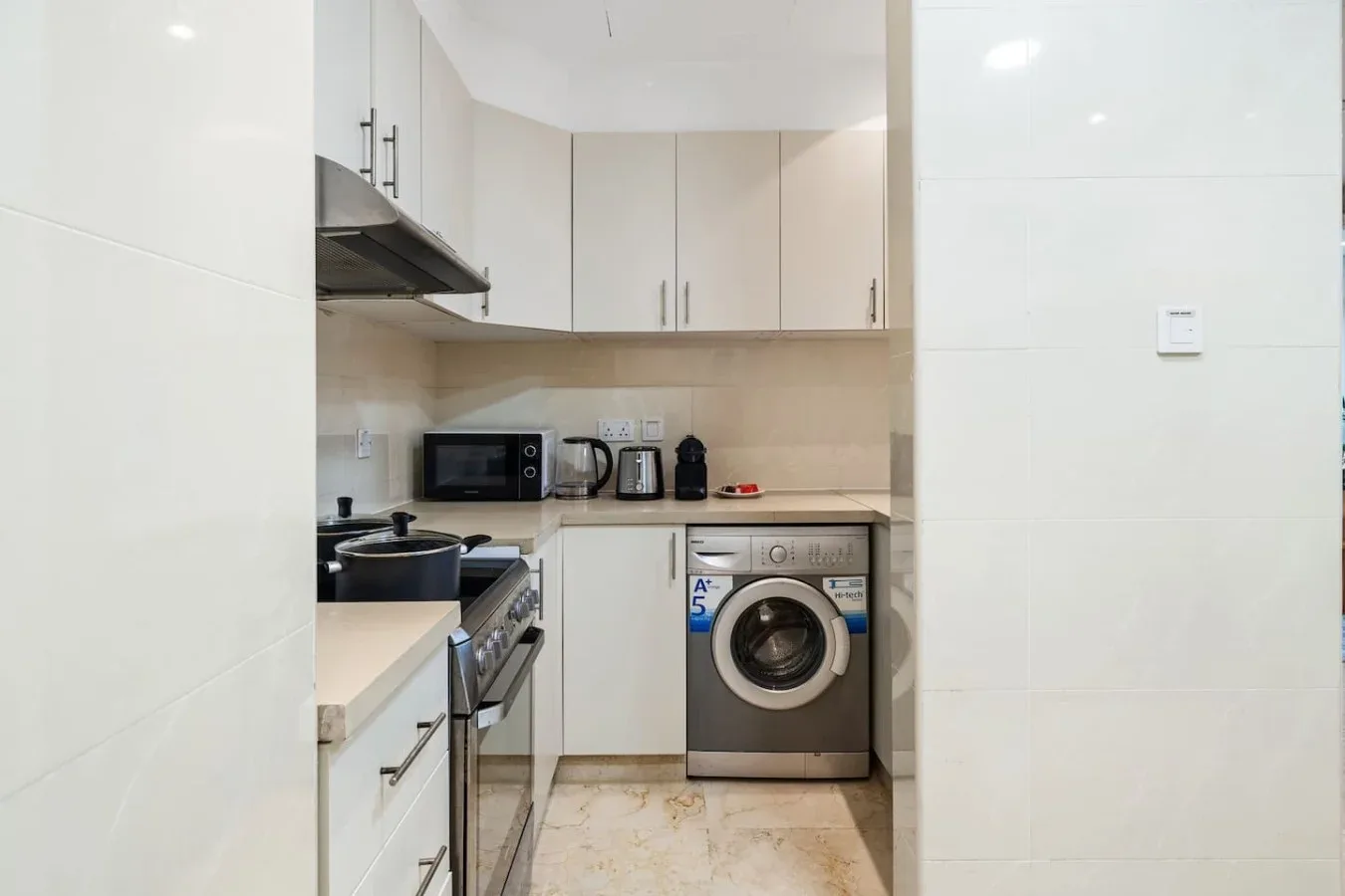 Una cocina compacta con gabinetes blancos, una estufa y una lavadora.
