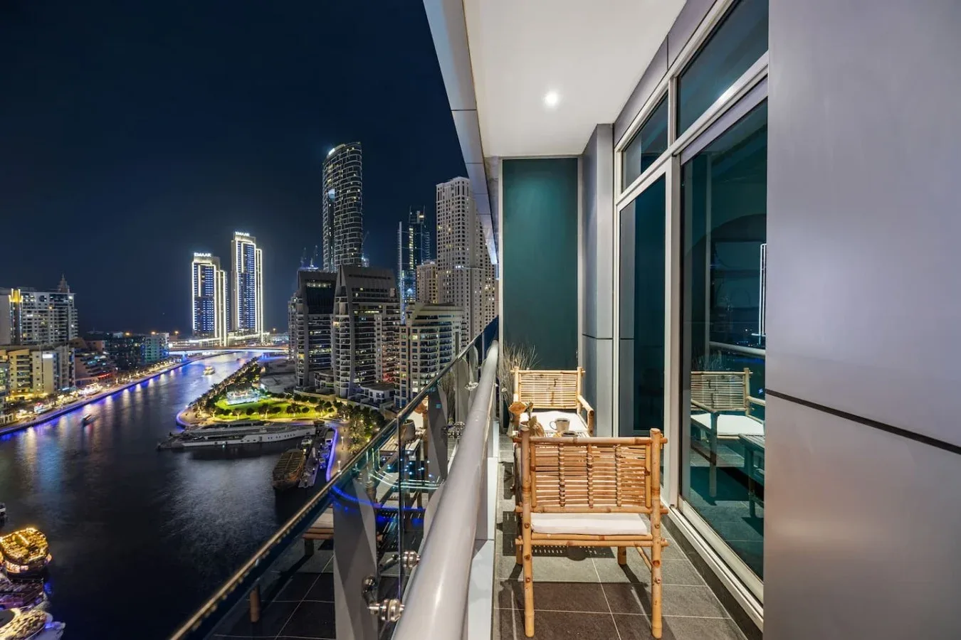 Una zona de estar en un balcón da a un horizonte urbano iluminado y un río de noche.