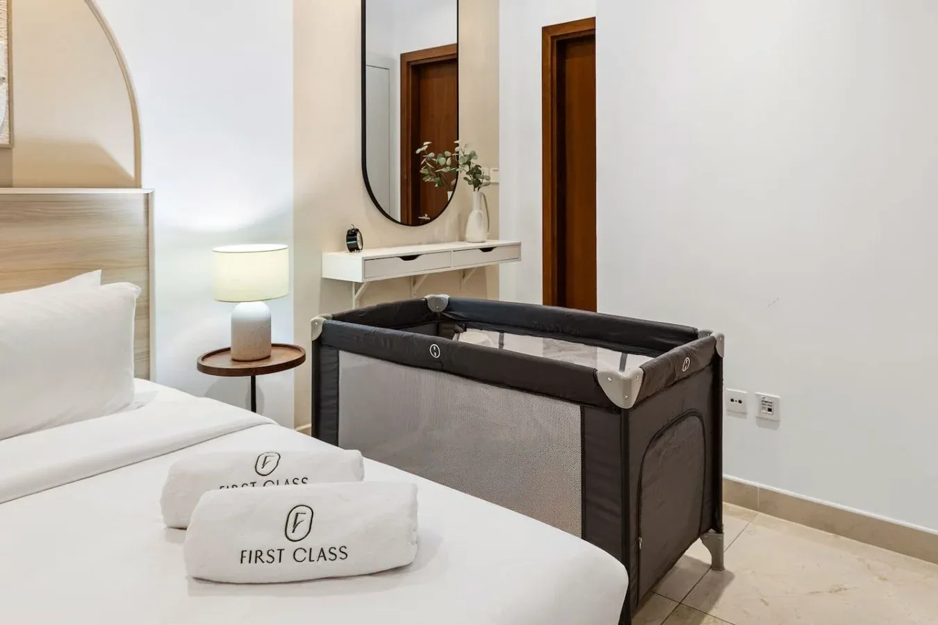 Un dormitorio con una cama, toallas dobladas y un corralito junto a la pared.