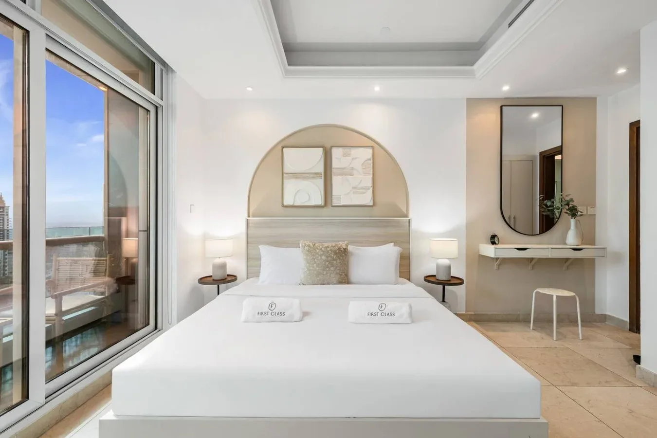 Un dormitorio luminoso con una cama bien tendida y grandes ventanales con vista al agua.