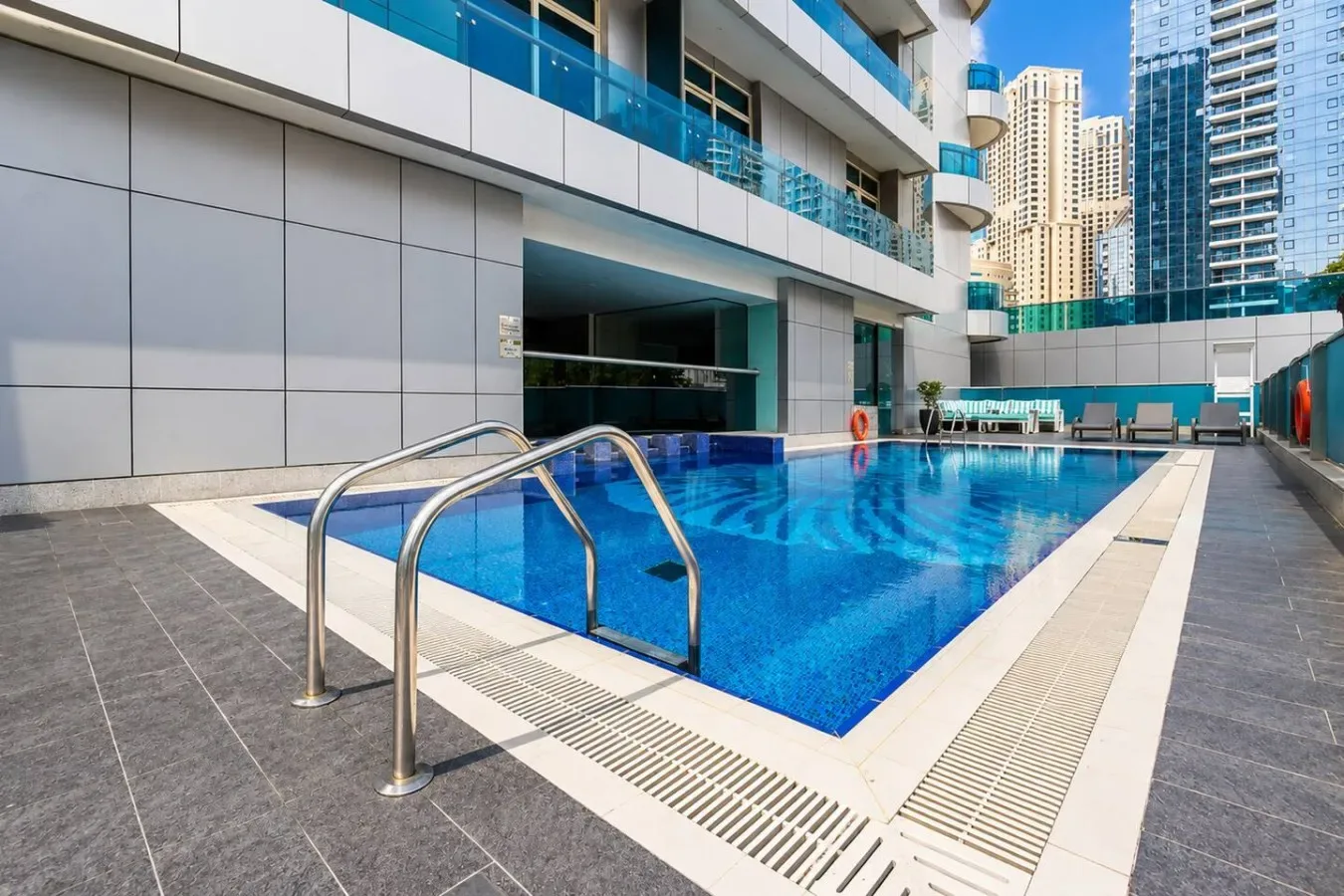 An outdoor swimming pool beside a modern building, with metal handrails at the edge.