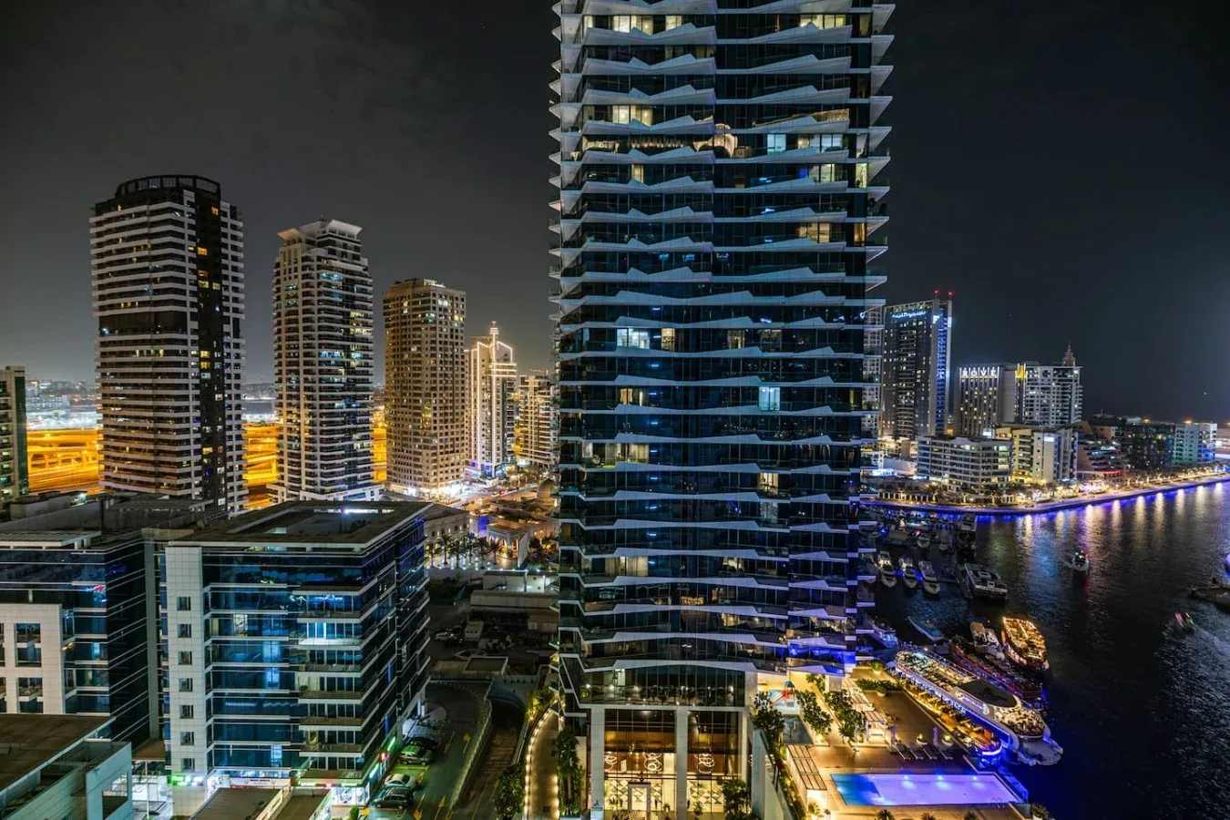 Un paisaje urbano nocturno muestra edificios altos iluminados junto a la costa.