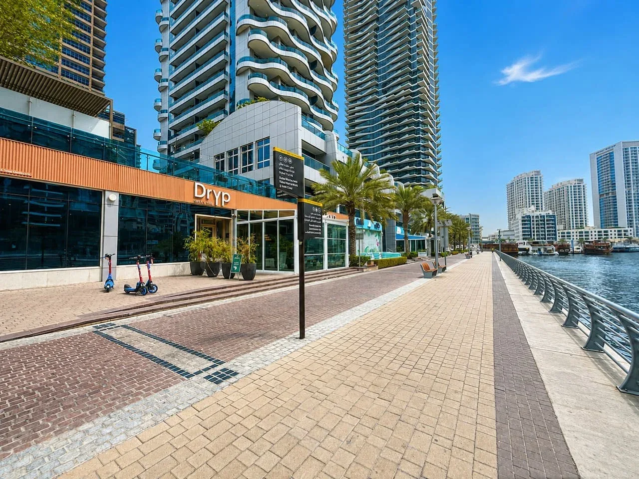 Un paseo pavimentado junto al agua bordea modernos edificios de gran altura.