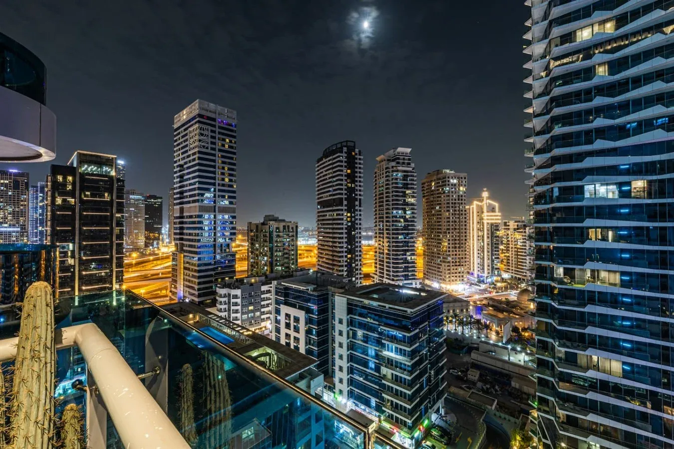 Un paisaje urbano nocturno visto desde un balcón, con edificios altos iluminados.