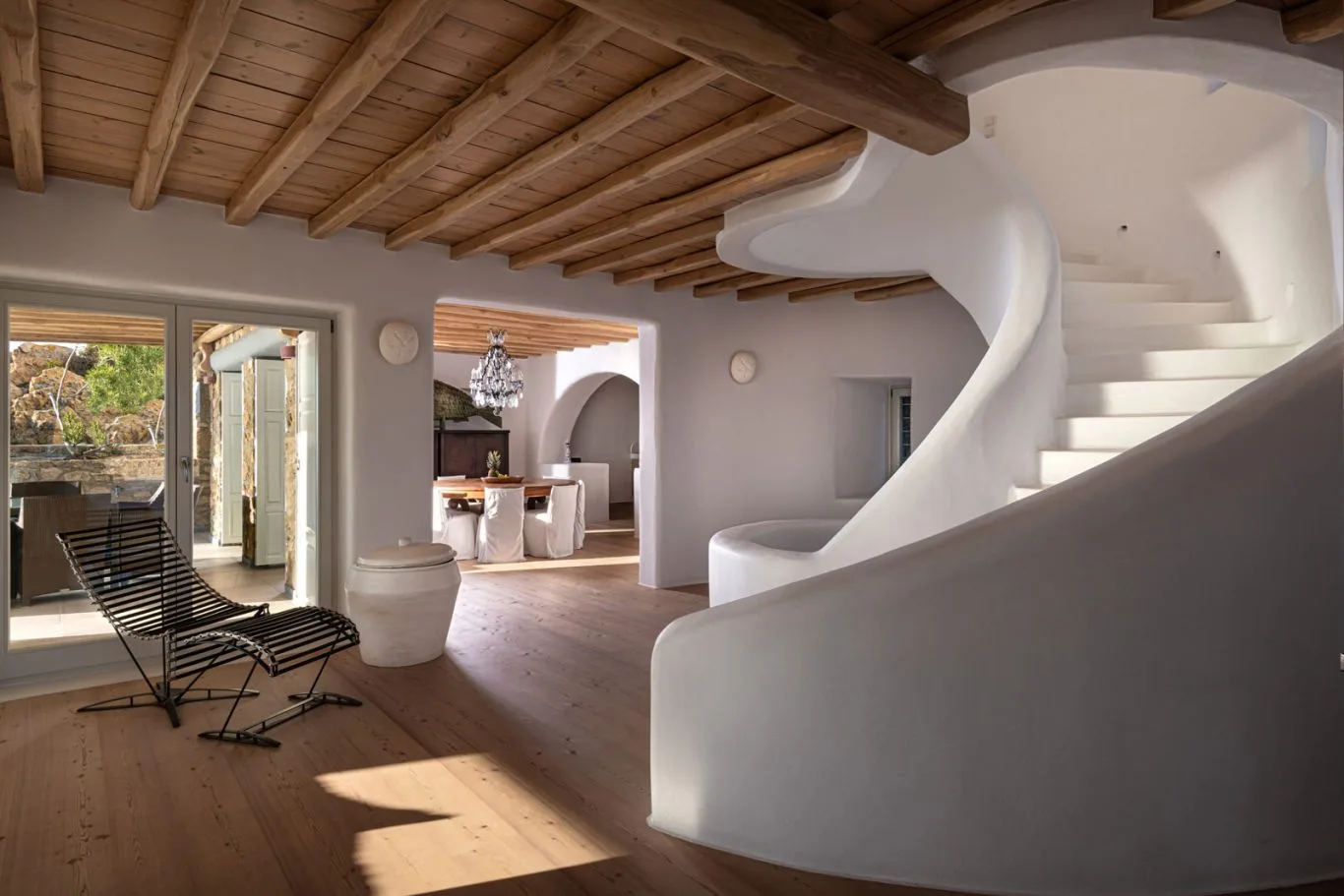 An open living area with a curved staircase and wooden ceiling beams.