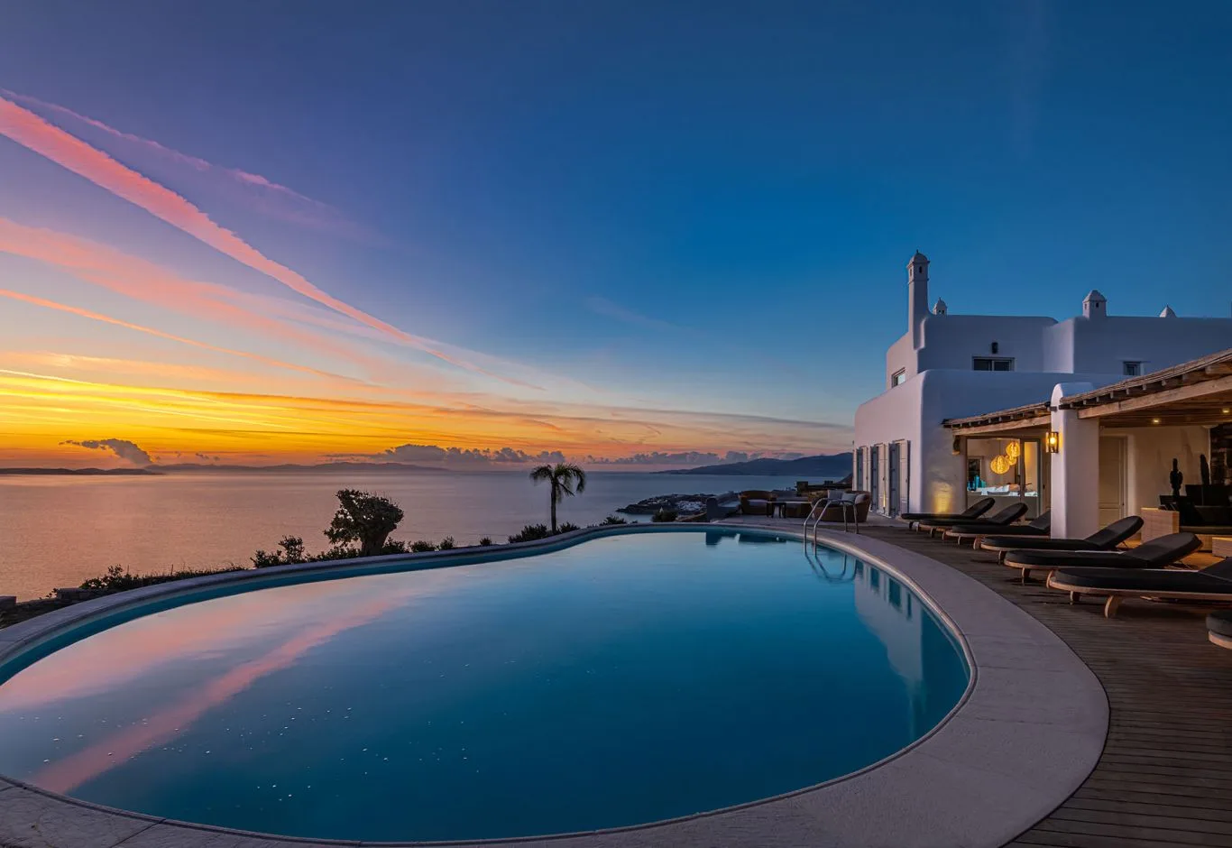 A curved swimming pool beside a white building at sunset.