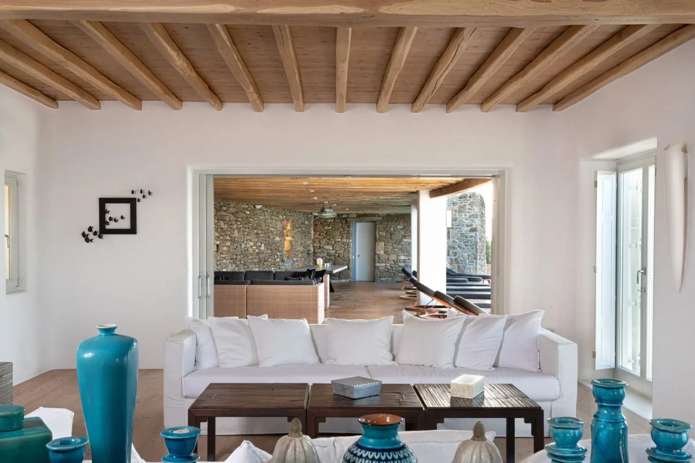 A bright living room with white seating and exposed wooden ceiling beams.