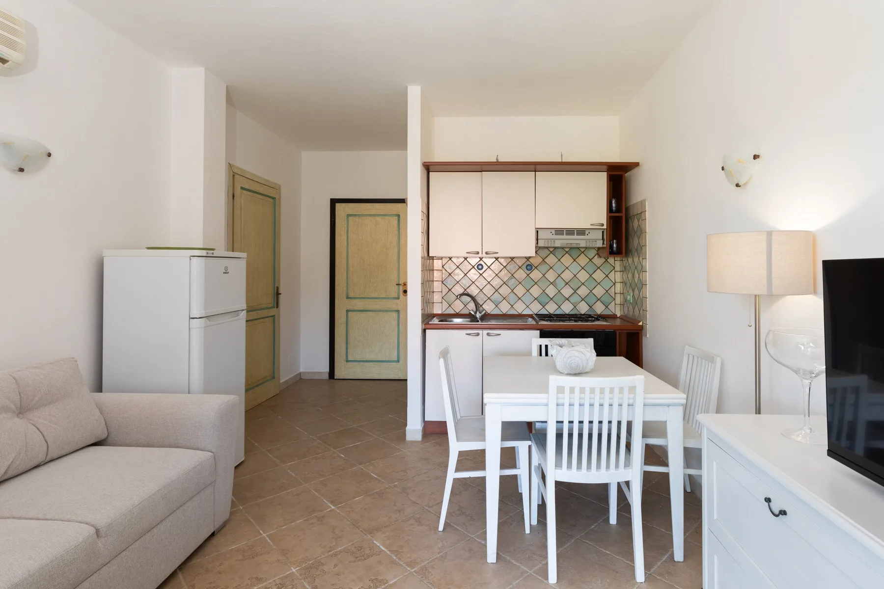 Comedor con mesa y sillas blancas junto a una cocina compacta.