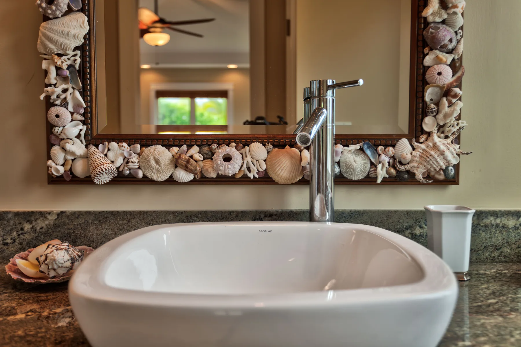 A bathroom vanity with a white basin beneath a shell-decorated mirror.